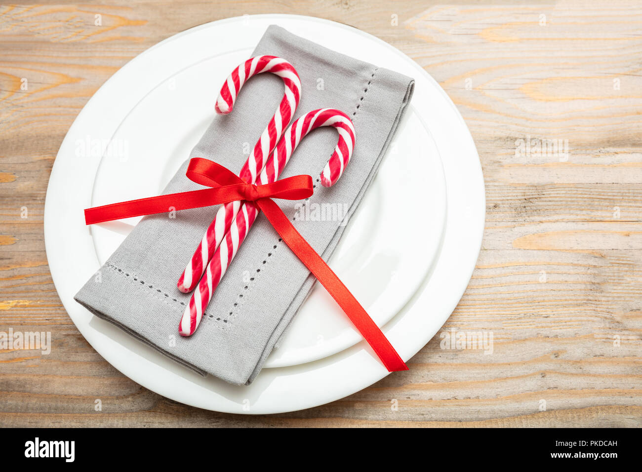Weihnachten Tabelle einstellen. Zuckerstangen und eine graue Serviette auf weiße Platten, Holz- Hintergrund Stockfoto