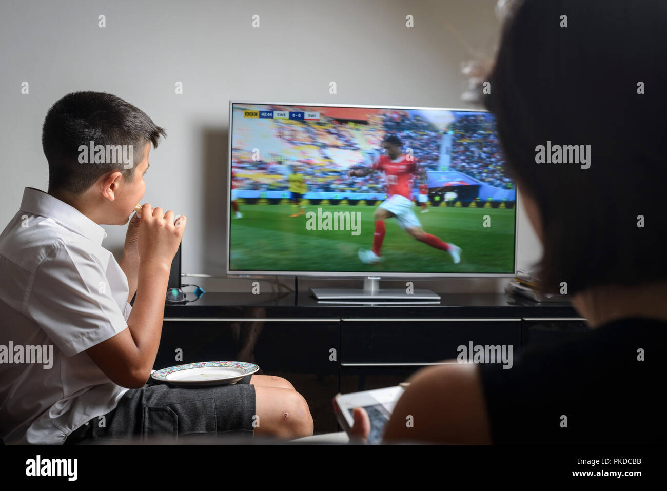 Schüler, die 10 Jahre alt, in Schuluniform Snacking und beobachten Fußballspiel im Fernsehen Stockfoto