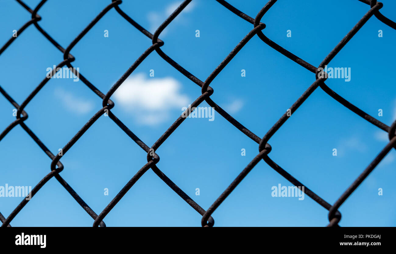 Selektiver Fokus auf Maschendrahtzaun mit blauem Himmel und Wolken im Hintergrund Stockfoto