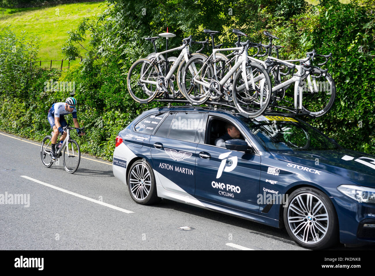 Man pro Fahrzeug mit Radfahrer hinter gehen durch Coniston auf der Tour 2018 von Großbritannien, Coniston, Cumbria, England, UK. Stockfoto