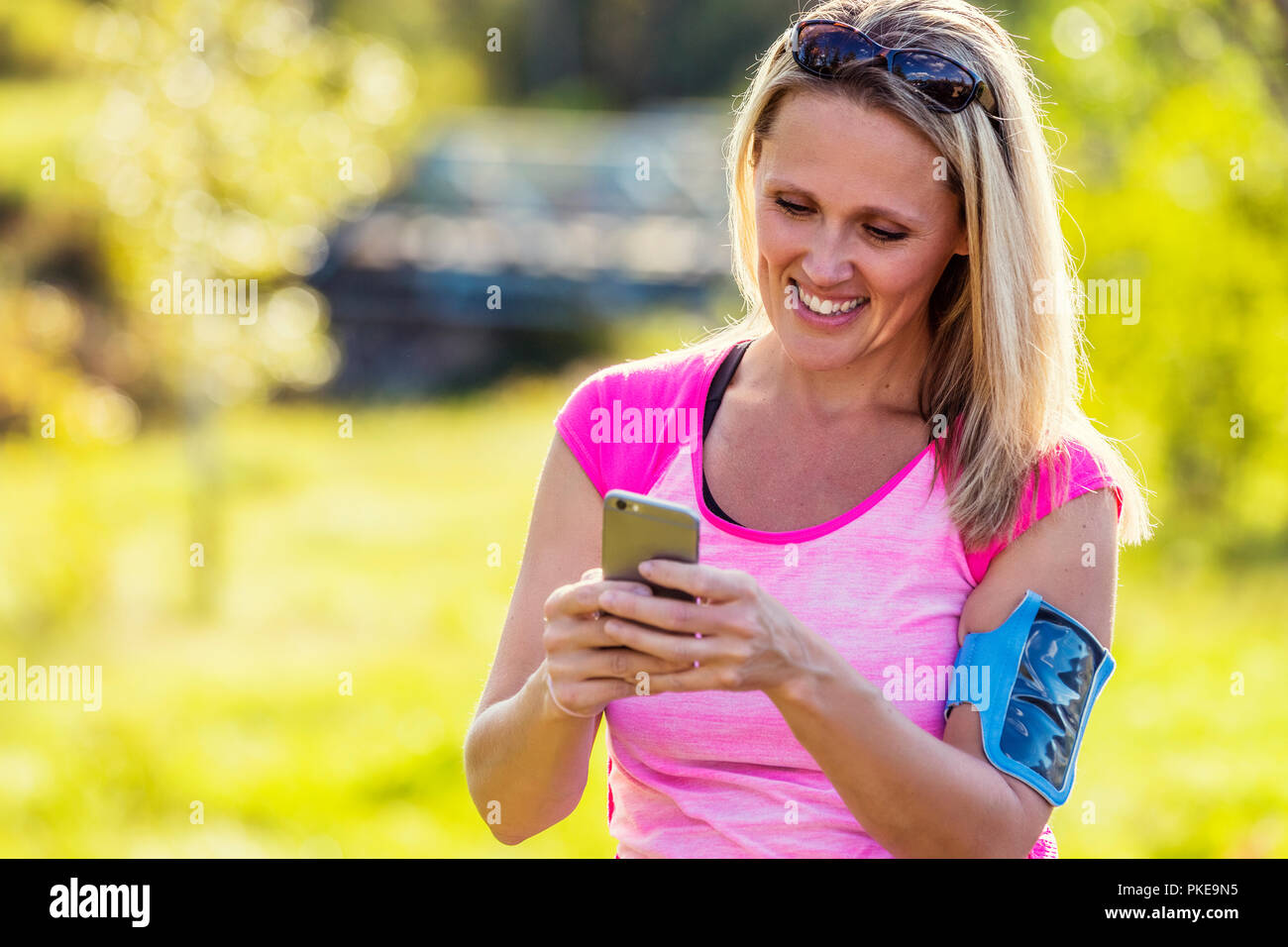 Eine reife Frau tragen aktiv tragen und ein Arm band ihr smart phone Texte, bevor Sie sich für einen Lauf in einem Stadtpark im Herbst Saison zu halten Stockfoto