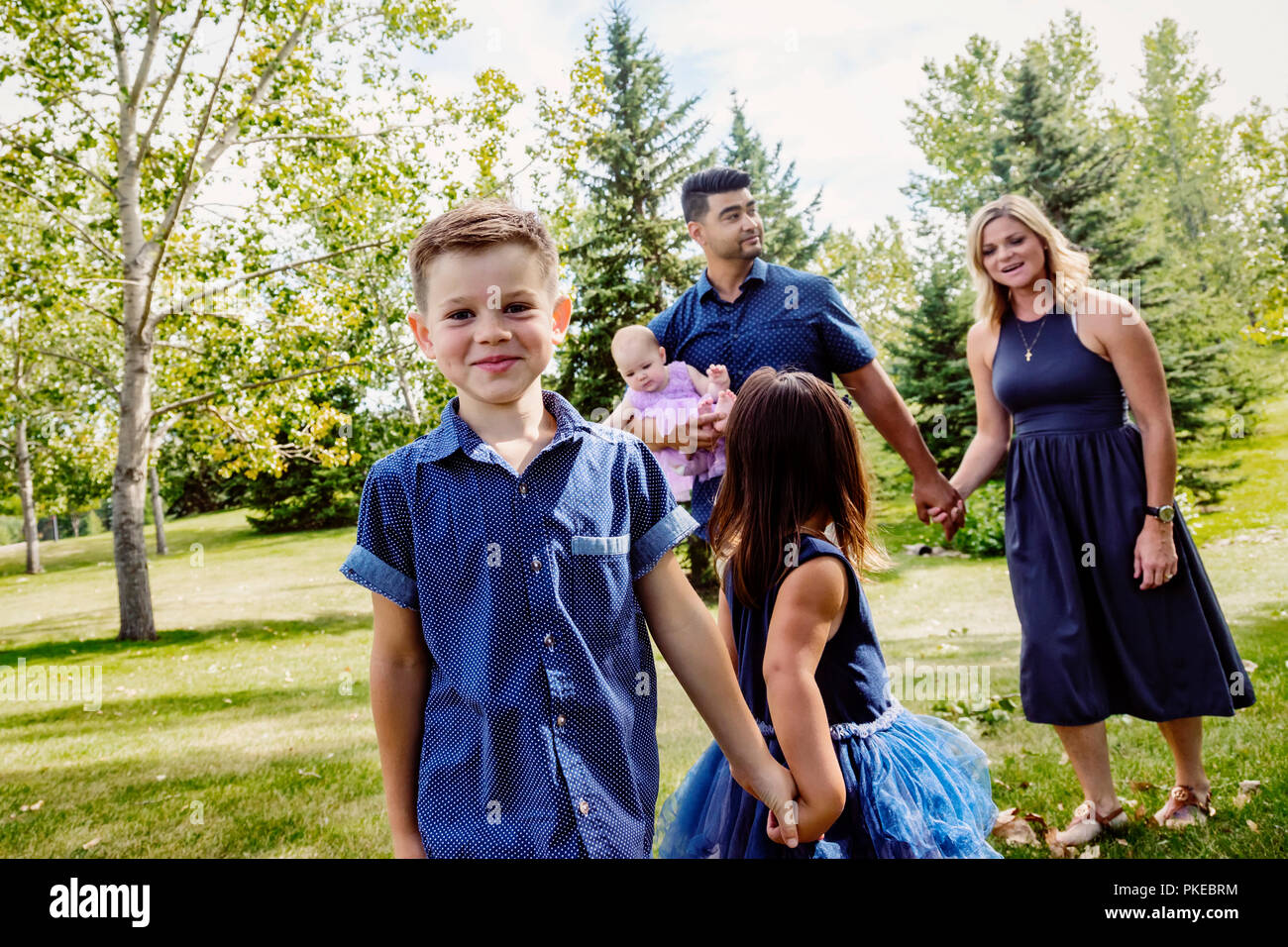 Eine Mutter und Vater in einer gemischten Rasse Ehe zu Fuß mit ihren Kindern in einem Park auf einem Familienausflug während eines warmen Herbsttag und ihr Sohn posiert für d... Stockfoto