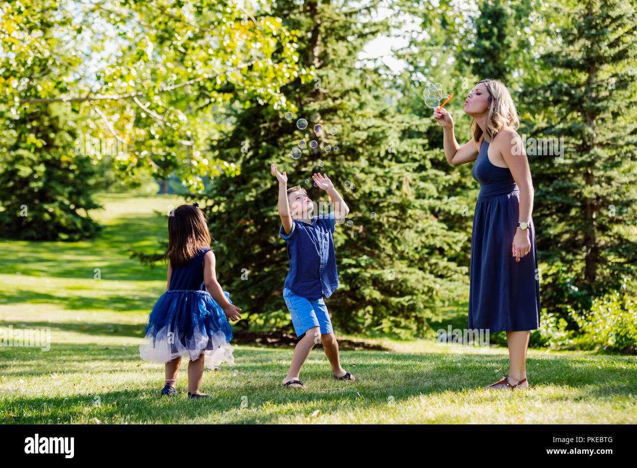 Eine Mutter blasen blasen für Ihre Kinder, während auf einem Familienausflug in einem Park auf einem warmen Herbst Tag; Edmonton, Alberta, Kanada Stockfoto