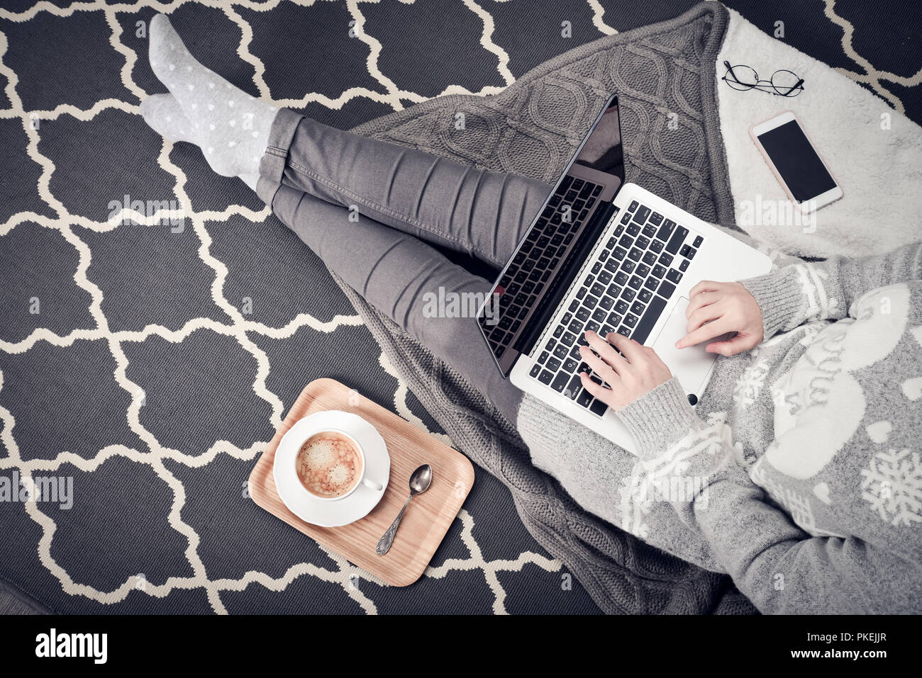 Junge kreative Frau auf dem Boden sitzen und arbeiten mit Laptop, Tasse Kaffee und Handy, Ansicht von oben Stockfoto