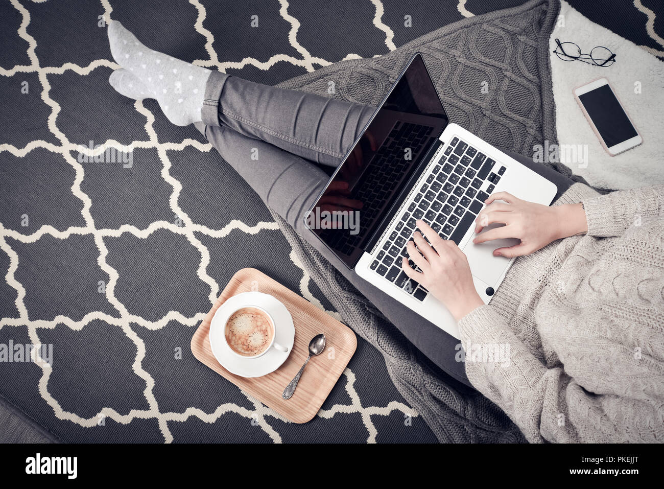 Junge kreative Frau auf dem Boden sitzen und arbeiten mit Laptop, Tasse Kaffee und Handy, Ansicht von oben Stockfoto