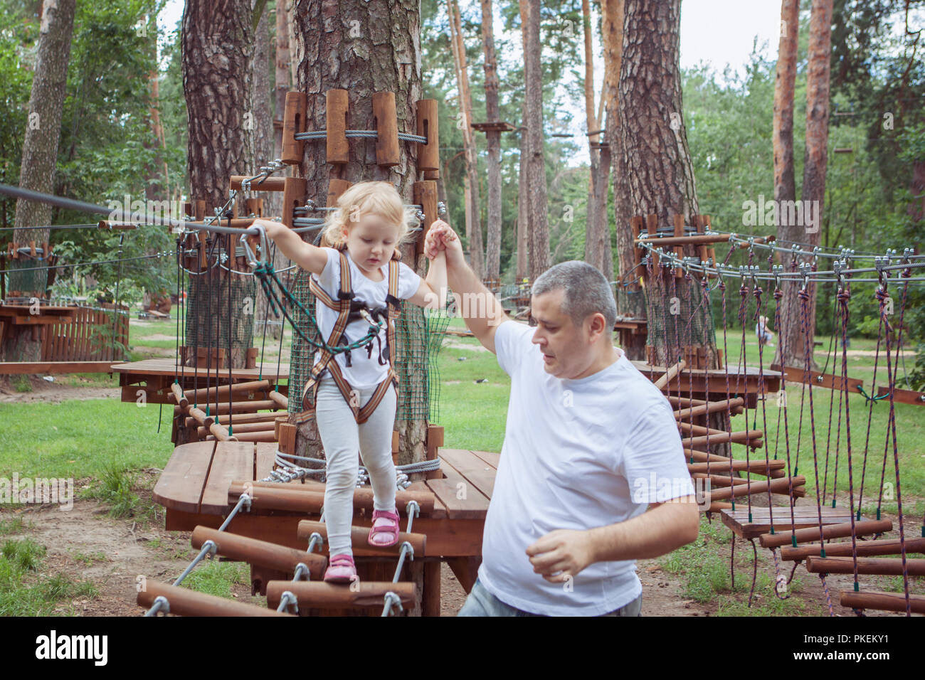 Kleines Mädchen mit ihrem Vater überwindet ein Hindernis im Seilpark. Stockfoto