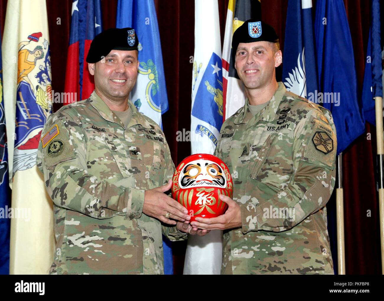 Command Sgt. Maj. Billy J. Norman, U.S. Army Garrison Japan command Sergeant Major und Oberst Phillip K. Gage, garrison Commander, präsentieren die Daruma Puppe zu jenen, die am 10.08.Übernahme von Verantwortung Zeremonie anwesend sind, im Camp Zama Gemeinschaft Club. Daruma, einem Japanischen Symbol von Glück ist durch eine gewichtete unten geprägt, so dass es immer wieder in eine aufrechte Position, wenn es ist umgekippt. Die Augen eines neuen Daruma sind unlackiert. Die Person, die Farben in einem Auge beim Beten für die Erfüllung von einigen besonderen Wünschen. Sie legen Sie dann die Daruma in der Familie Schrein oder die Stockfoto