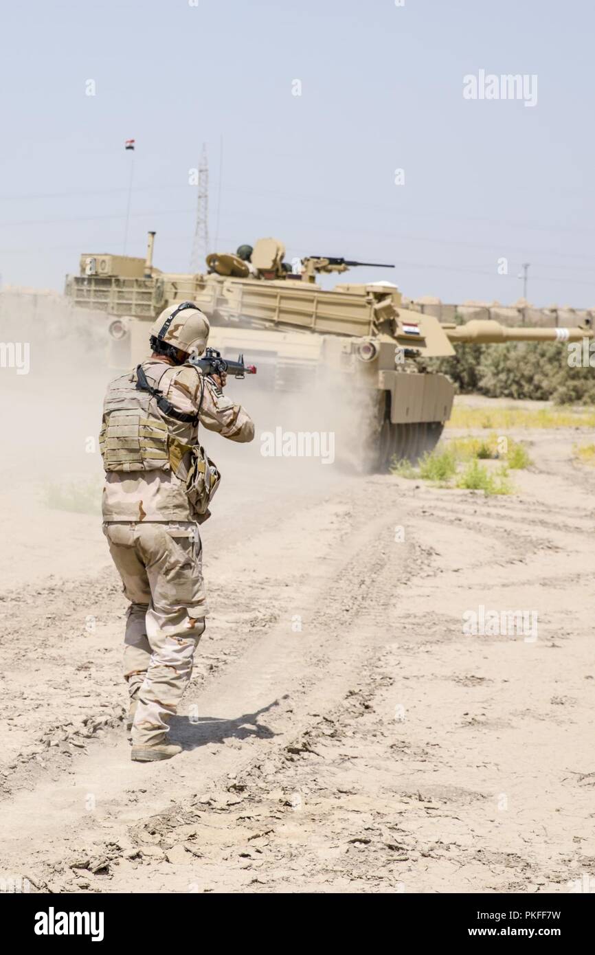 Ein irakischer Soldat, mit 2Nd Battalion, 59th Brigade, Patrouillen hinter einem M1A1 Abrams Tank während einer bestätigenden Ausbildungstätigkeit an Camp Taji, Irak, 30. Juli 2018. Durch beschleunigte Erfolge gegen ISIS im Jahr 2017 aktiviert, Koalition Unterstützung für unsere Partner entwickelt, wie wir unsere Partner bei der Bereitstellung von Sicherheit, die Stabilisierung unterstützen. Stockfoto