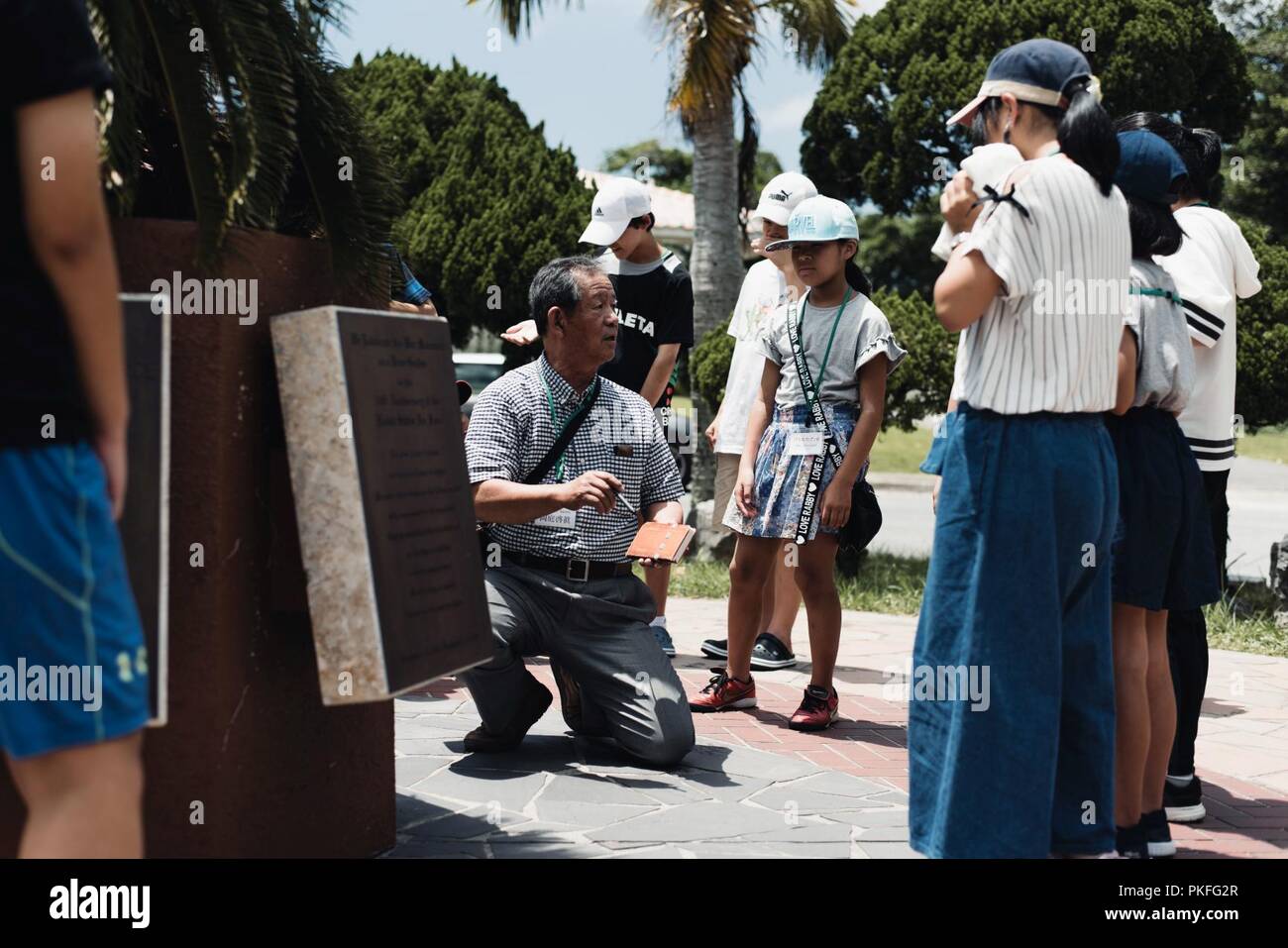 Die Teilnehmer sammeln sich um ihr Ausbilder, da sie sich auf den Zweiten Weltkrieg Geschichtsunterricht Aug 6, 2018, bei Kadena Air Base, Japan hören. Kinder aus beiden Achi Dorf Shimoina Bezirk, Präfektur Nagano und Okinawa City, Japan, besucht Kadena Air Base als Teil ihrer Bildung für den Frieden. Stockfoto