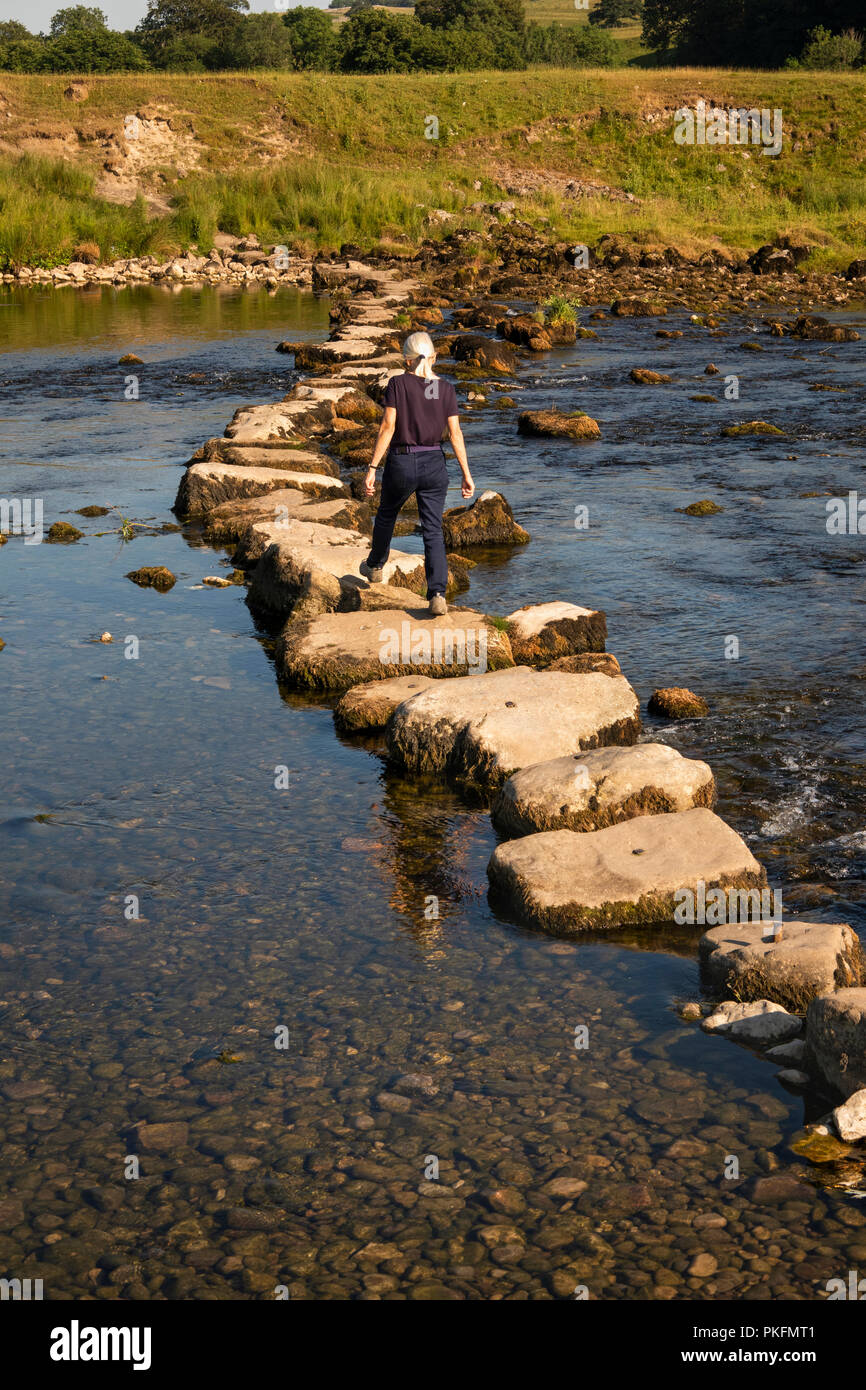 England, Yorkshire, Wharfedale, Grassington, Frau mit Stepping Stones über River Wharfe während der trockenen Sommer Wetter Stockfoto