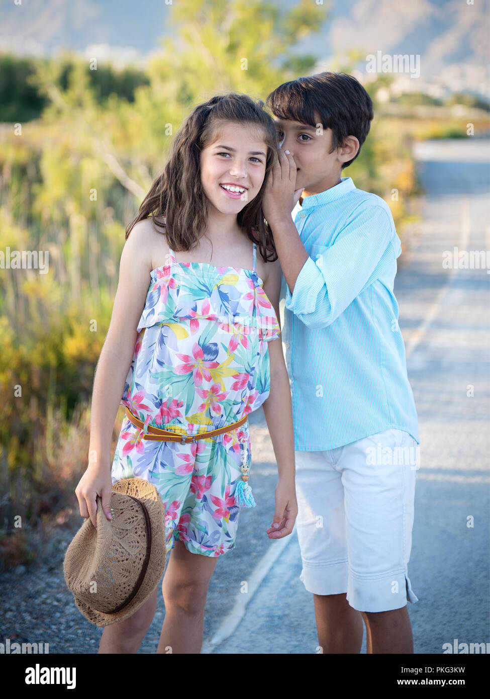 Fröhlicher Junge und Mädchen whispering gegen Natur Hintergrund Stockfoto