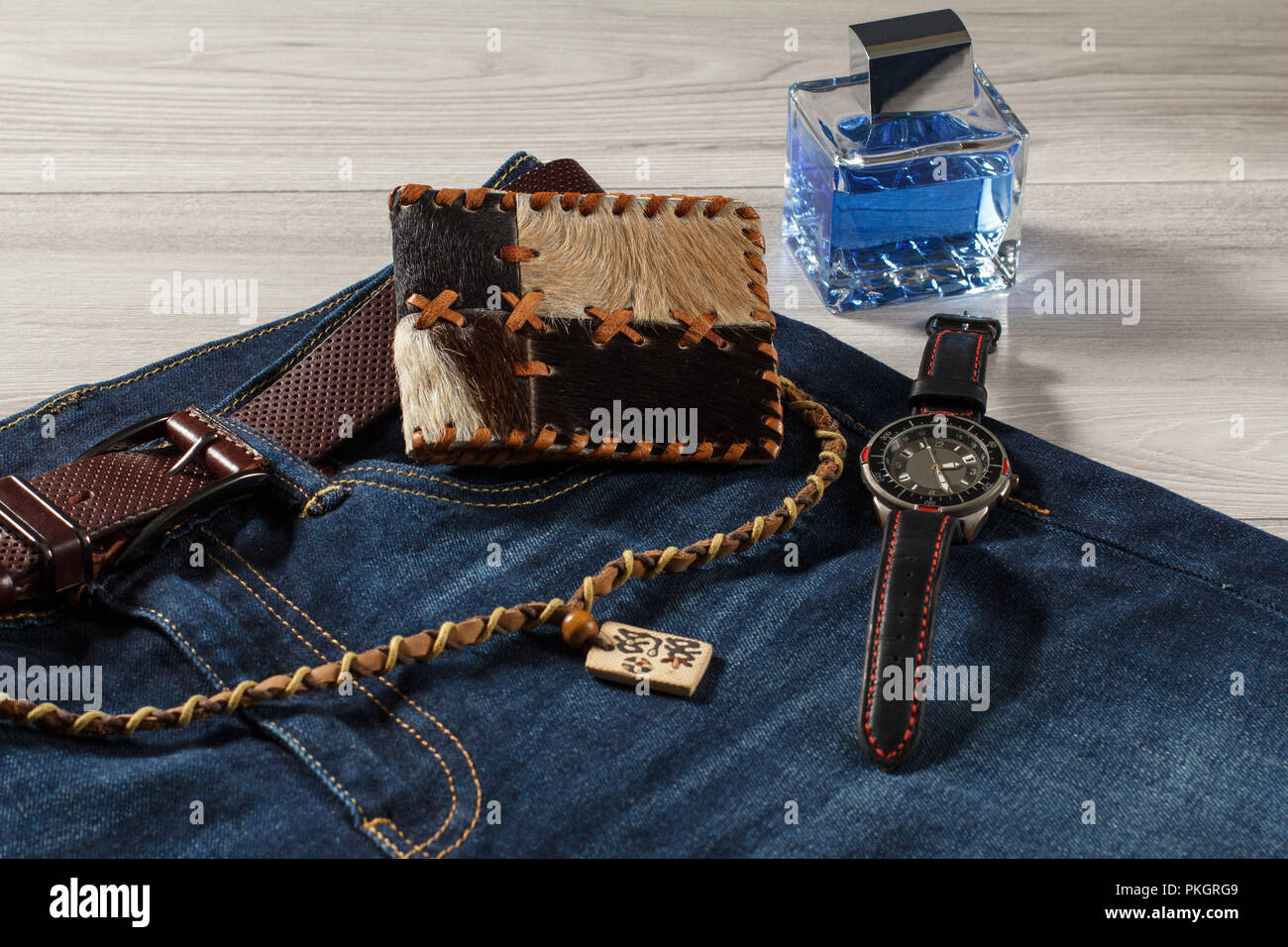 Man Parfum, Uhren mit Lederband, Jeans mit Leder Gürtel, Leder Geldbörse  und Amulett auf grauem Hintergrund Holz Stockfotografie - Alamy