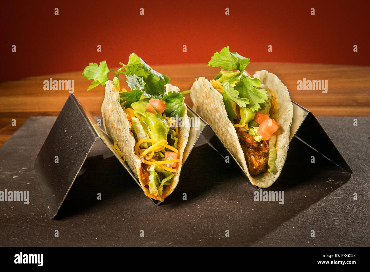 Zog Schweinefleisch Taco auf Edelstahl Ständer mit einem roten Hintergrund auf einem Stein und Holz Tisch. Fotografie von Arpi Pap Stockfoto