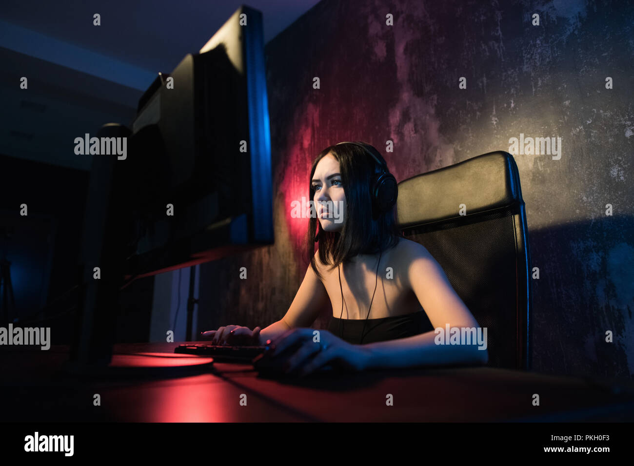 Portraitfotos mit einem lächelnden Schönen professionelle Gamer Mädchen spielen in First Person Shooter Online Video Spiel auf Ihrem eigenen Computer. Lässig süß Geek sprechen in Headset Stockfoto