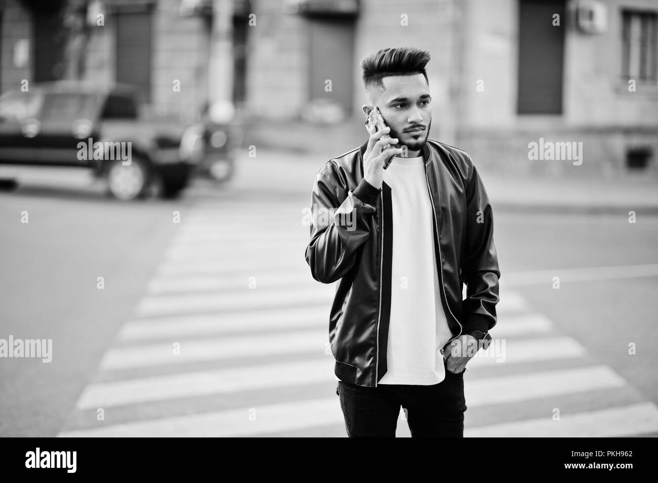 Stilvolle indischen Bart Mann an schwarze Lederjacke zu Fuß auf Zebrastreifen. Indien Modell stellte im Freien an Straßen der Stadt und sprechen. Stockfoto