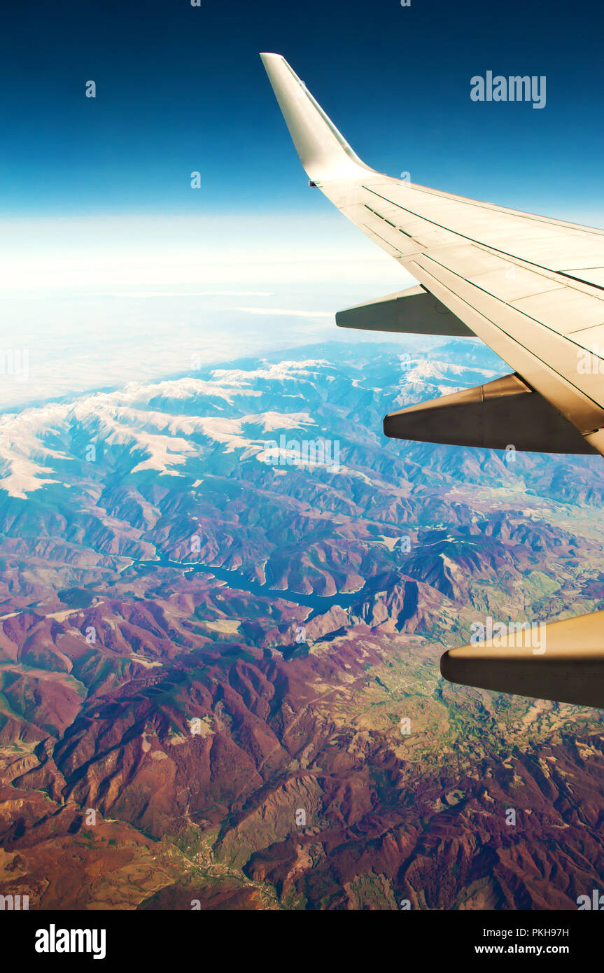 Weiß Flugzeugflügel. Luftaufnahme von majestätischen Gebirge mit gelben Spitzen, grünen und roten Wald, Felder, blauer Himmel und Horizont. Sonnigen, wolkenlosen aut Stockfoto