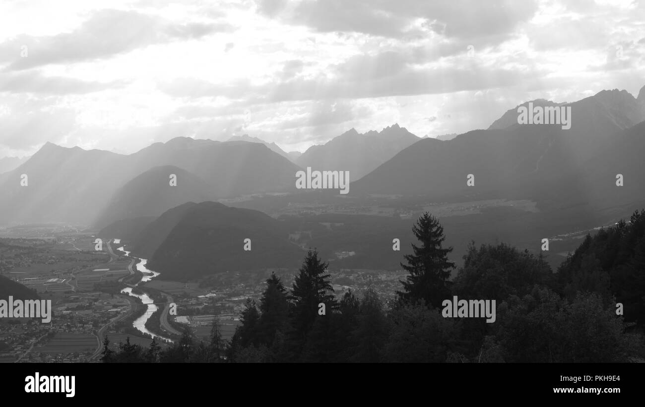 Schwarze und weiße Blick auf die österreichischen Alpen und das Tal in der Region Tirol mit Sonnenstrahlen und gewundenen Fluss und Bäume. Stockfoto