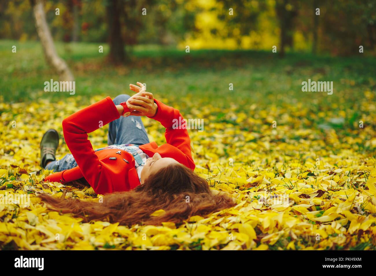 Lächelnde Mädchen mit langen gewelltem Haar das Leben geniessen im Herbst Wald. Fröhliches schönes Mädchen in Rot cout und bunten Plaid Shirt auf schönen Herbst Tag. Werden Stockfoto