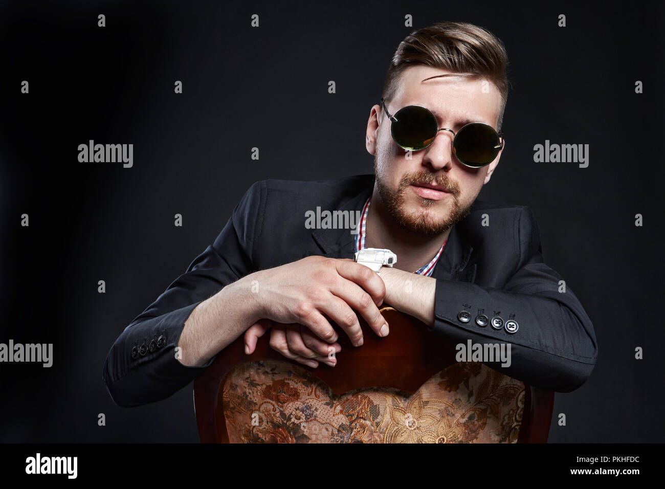 Mann in der Brille sitzt auf einem Stuhl. Unternehmer zuversichtlich Mann. SEO Manager posieren auf einem schwarzen Hintergrund. Erfolgreiche Unternehmer Stockfoto