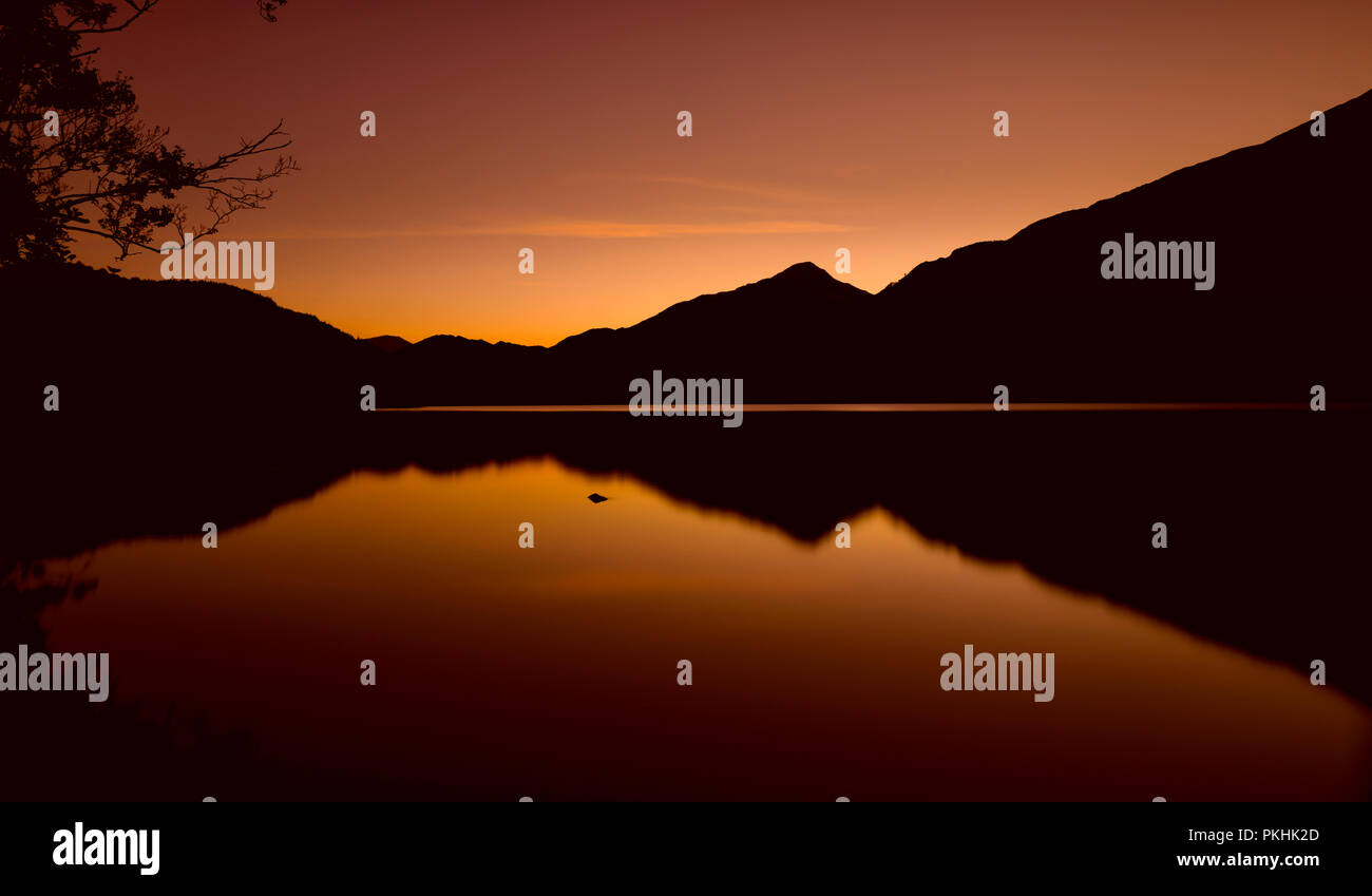 Die Sonne ist hinter den Bergen um Llyn Gwynant, ein See in Snowdonia (Eryri), Wales (Cymru), UK. Ein verbrannter Himmel silhouetting die Berge, Cast Stockfoto