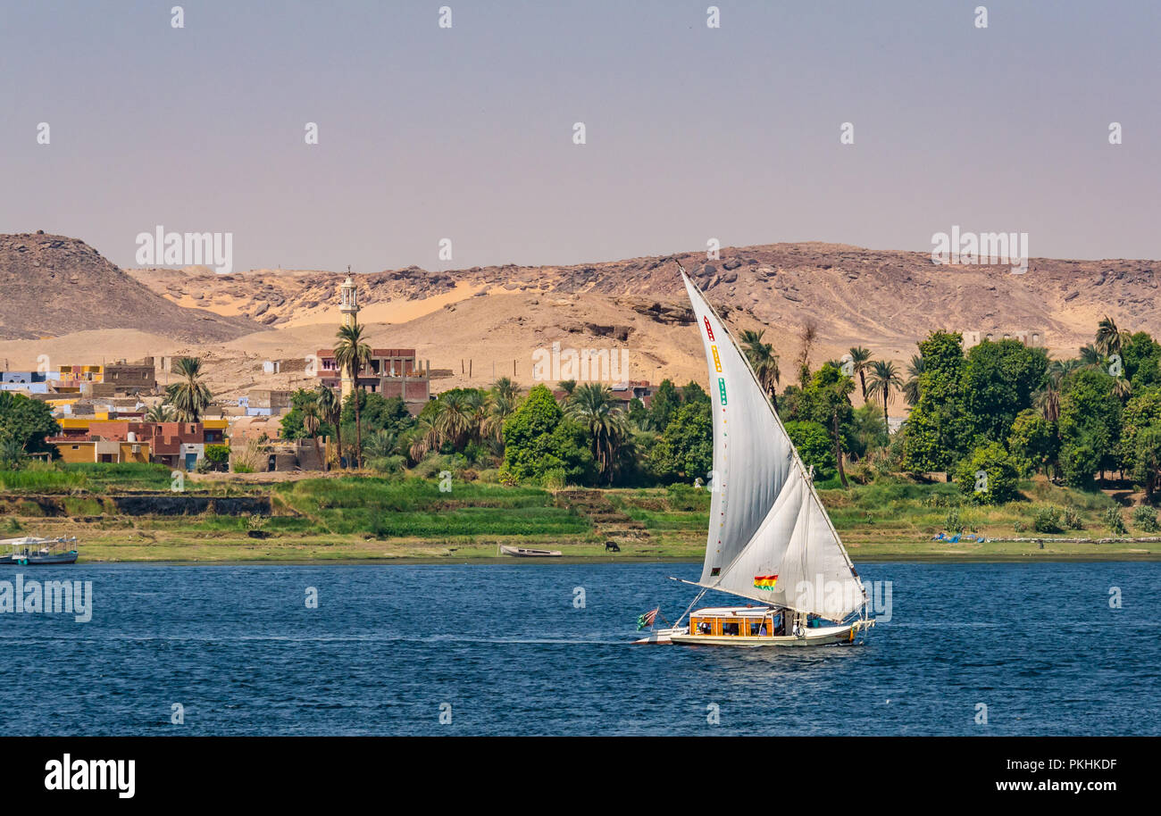Traditionelle felucca Segelboot mit Blick auf die West Bank, Moschee Minarett und Sand Felsen, Nil, Assuan, Ägypten, Afrika Stockfoto
