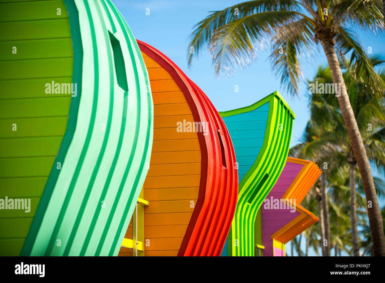 Abstrakte Reihe von bunt bemalten bunte Rettungstürme mit Kokospalmen am Miami Beach Promenade. Stockfoto
