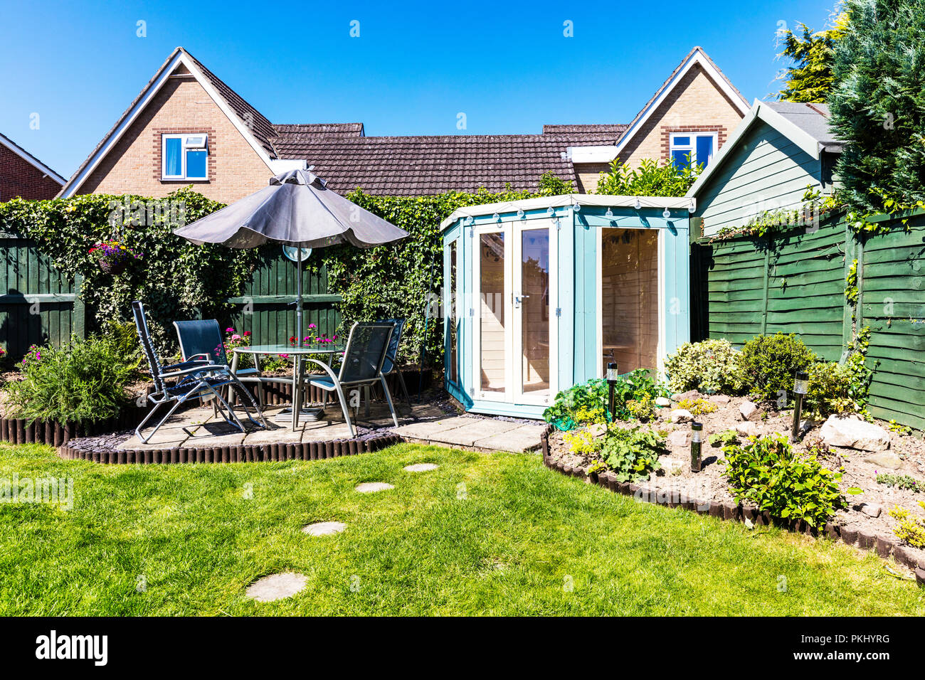 Englischer Garten, Gartenhaus, Terrasse, Tisch und Stühle draußen, umzäunter Garten, Trittsteine, Regenschirm über Tabelle, Sommerhäuser, UK, England, Stockfoto