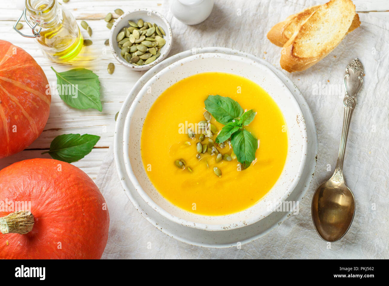 Ernährung Vegetarische Kürbis creme Suppe pürieren, mit Olivenöl, Samen und Basilikum auf einem hölzernen Tisch in eine weiße Platte. Selektiver Fokus Stockfoto