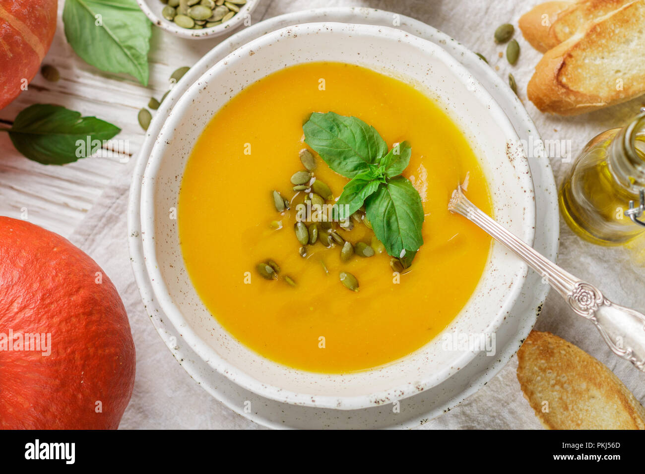 Ernährung Vegetarische Kürbis creme Suppe pürieren, mit Olivenöl, Samen und Basilikum auf einem hölzernen Tisch in eine weiße Platte. Selektiver Fokus Stockfoto