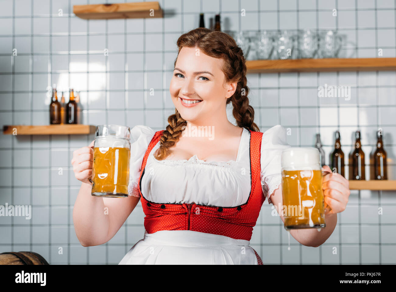 Happy oktoberfest Kellnerin im traditionellen bayerischen Kleid zeigen Becher helles Bier in der Nähe von bar Counter Stockfoto