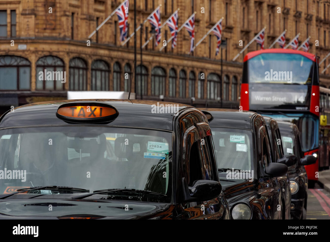 Schwarze Taxi-Taxis auf der Brompton Road in Knightsbridge mit Harrods Kaufhaus im Hintergrund, London England Großbritannien Stockfoto