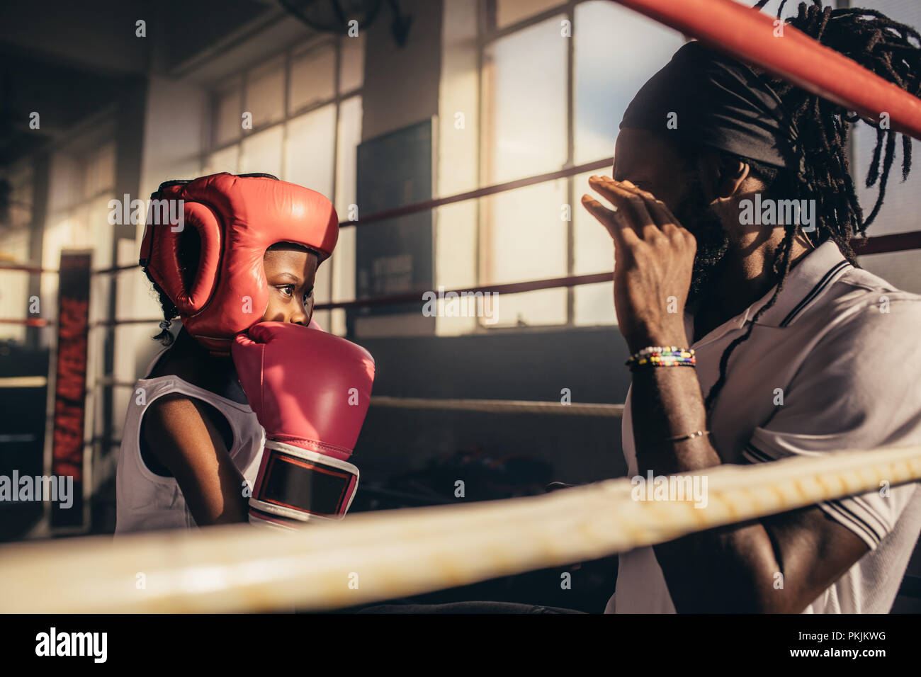 Boxtrainer erteilen Anweisungen an ein Kind zu einem Boxing Gym. Kid Boxhandschuh und Kopfbedeckungen Training mit seinem Trainer in einem Boxring. Stockfoto