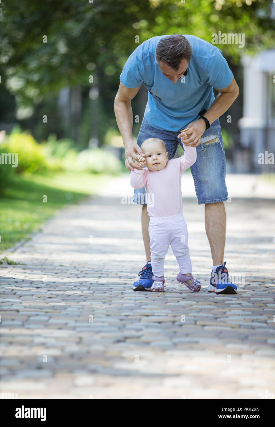 Vater, Tochter und helfen, ihre ersten Schritte machen. Vater und Tochter auf Spaziergang im Sommer Park. Stockfoto