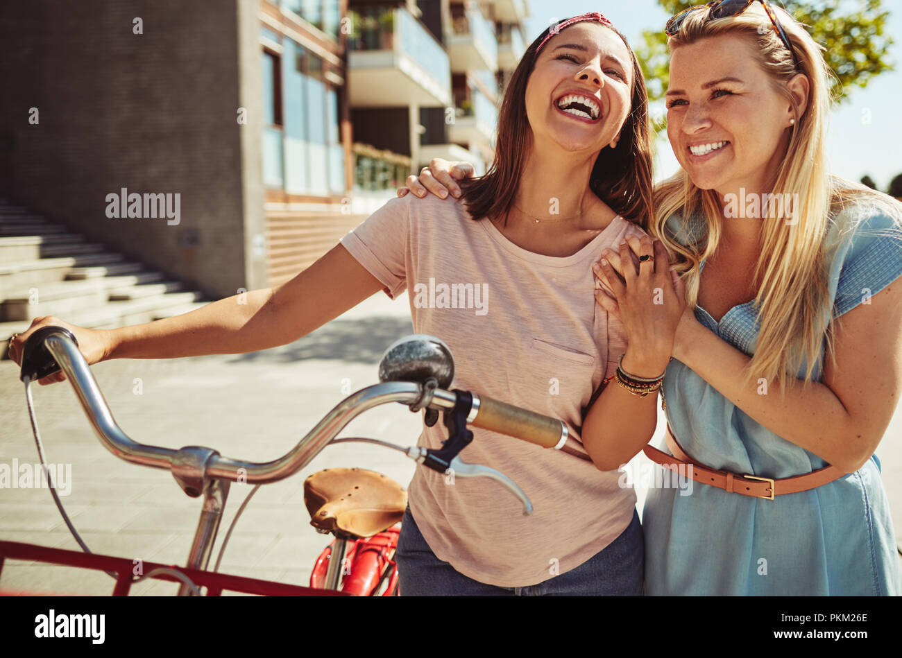 Zwei junge weibliche Freunde, durch die Stadt zu gehen und mit ihrem Fahrrad Lachen und Spaß zusammen Stockfoto