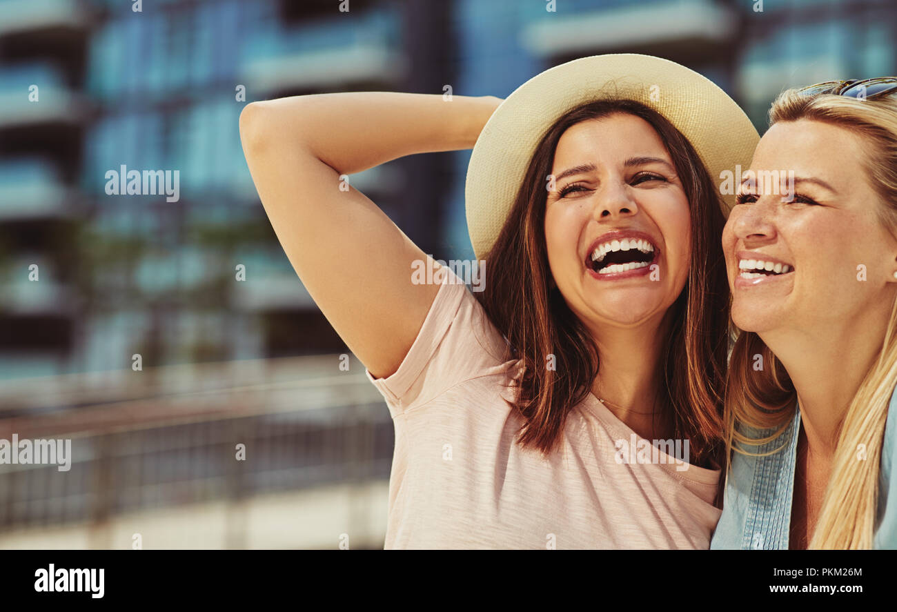 Zwei lachende Junge weibliche Freunde stehen Arm in Arm zusammen eine gute Zeit in der Stadt im Sommer Stockfoto