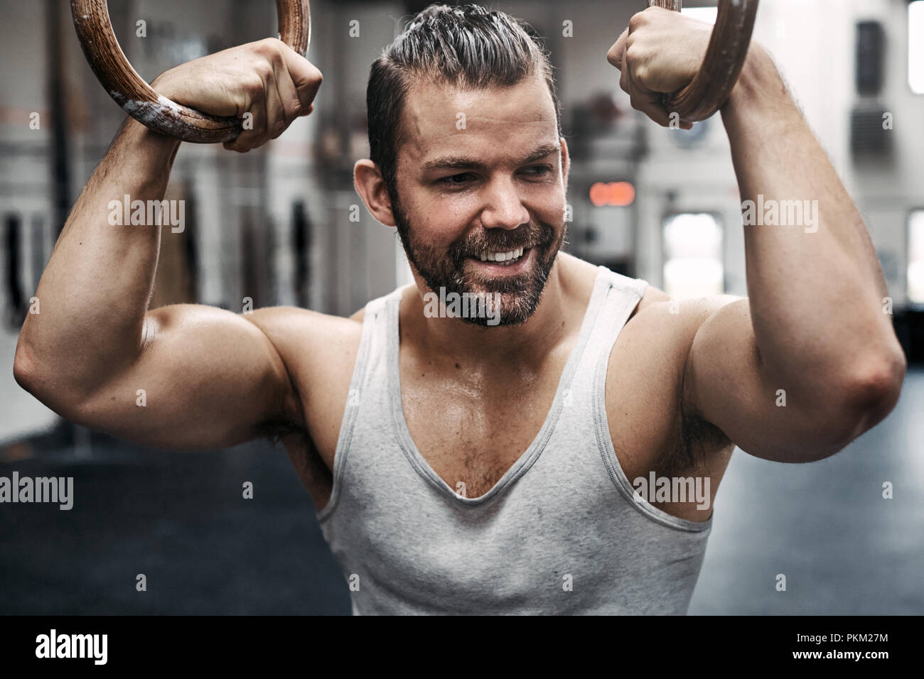 Passen junge Mann in Sportkleidung lächelnd, während Sie arbeiten einen Schweiß beim Training Session auf Ringe an einem Health Club Stockfoto