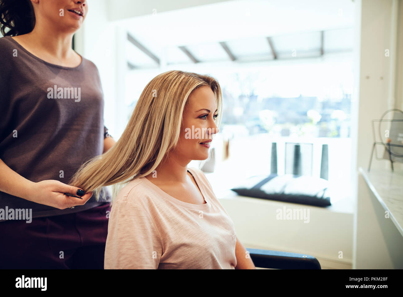 Lächelnde blonde junge Frau sitzt in einem Salon Stuhl in Ihr Haar bei einem Termin mit ihr Hairstylist getan Stockfoto