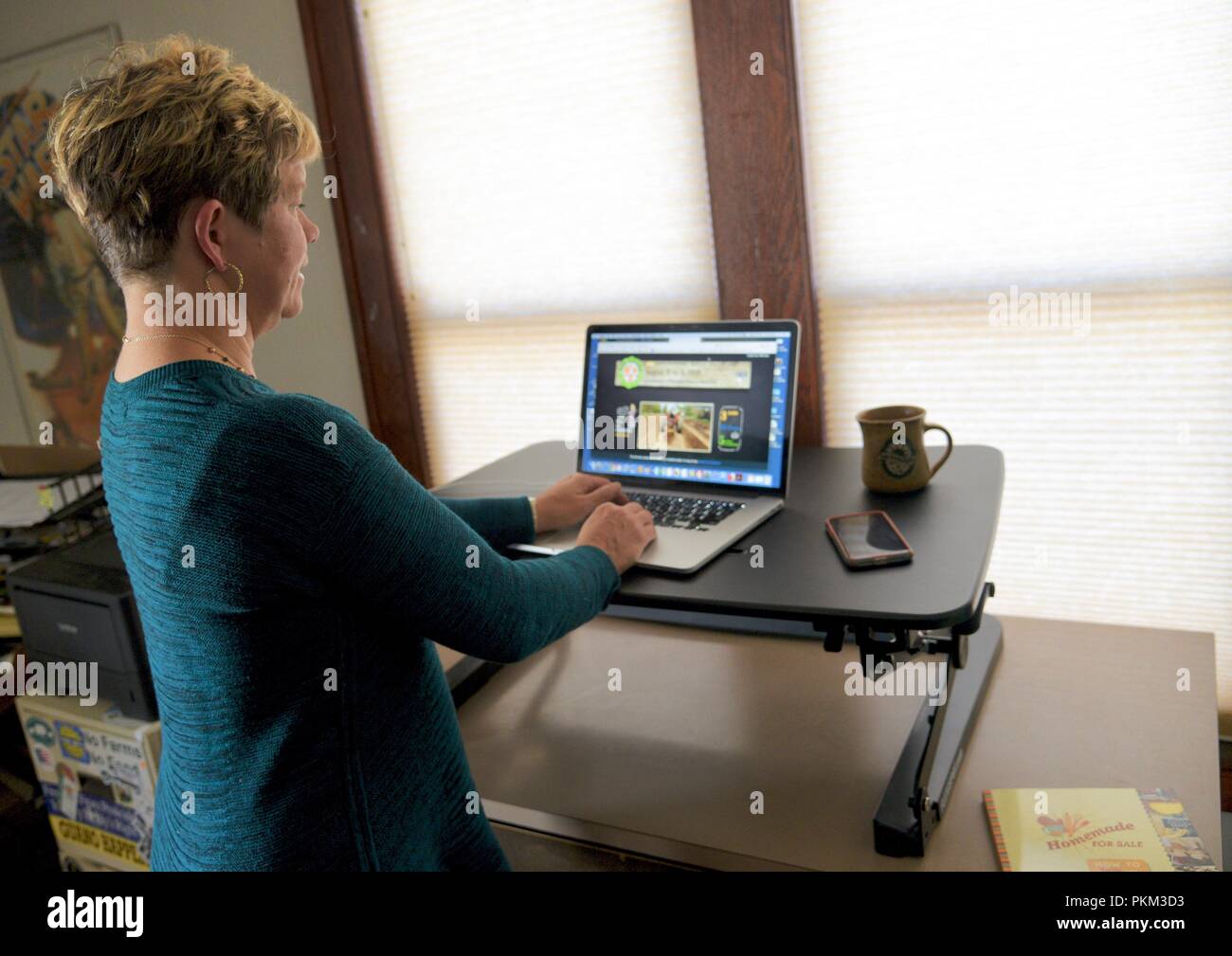 Mitte - Alter business Frau stehen und arbeiten an Apple MacBook Pro mit FlexiSpot/Loctek ergonomisches Stehpult im Büro zu Hause, Browntown, WI, USA Stockfoto