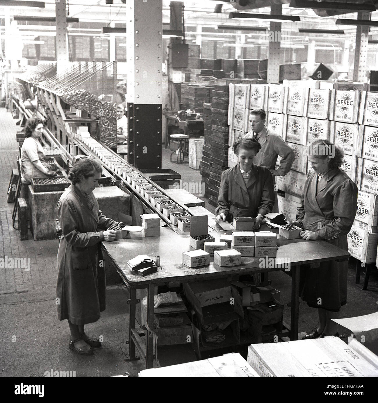 1950, historische, weibliche Arbeitnehmer in Latzhosen am Ende einer Produktion Verpackung Batterien in Boxen, London, England, UK. Stockfoto