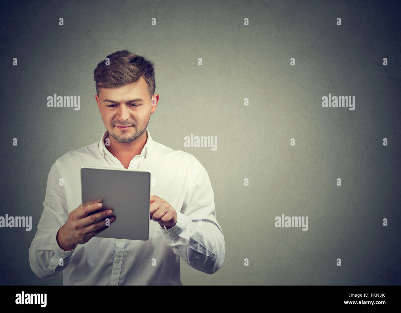Inhalt lässiger Kerl in weißem T-Shirt surfen modernen Tablet genießen neues Gerät auf Grau. Stockfoto