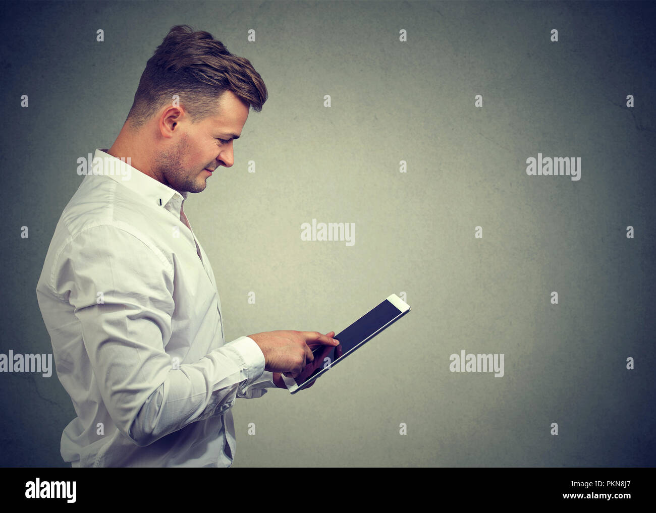 Inhalt lässiger Kerl in weißem T-Shirt surfen modernen Tablet genießen neues Gerät auf Grau. Stockfoto