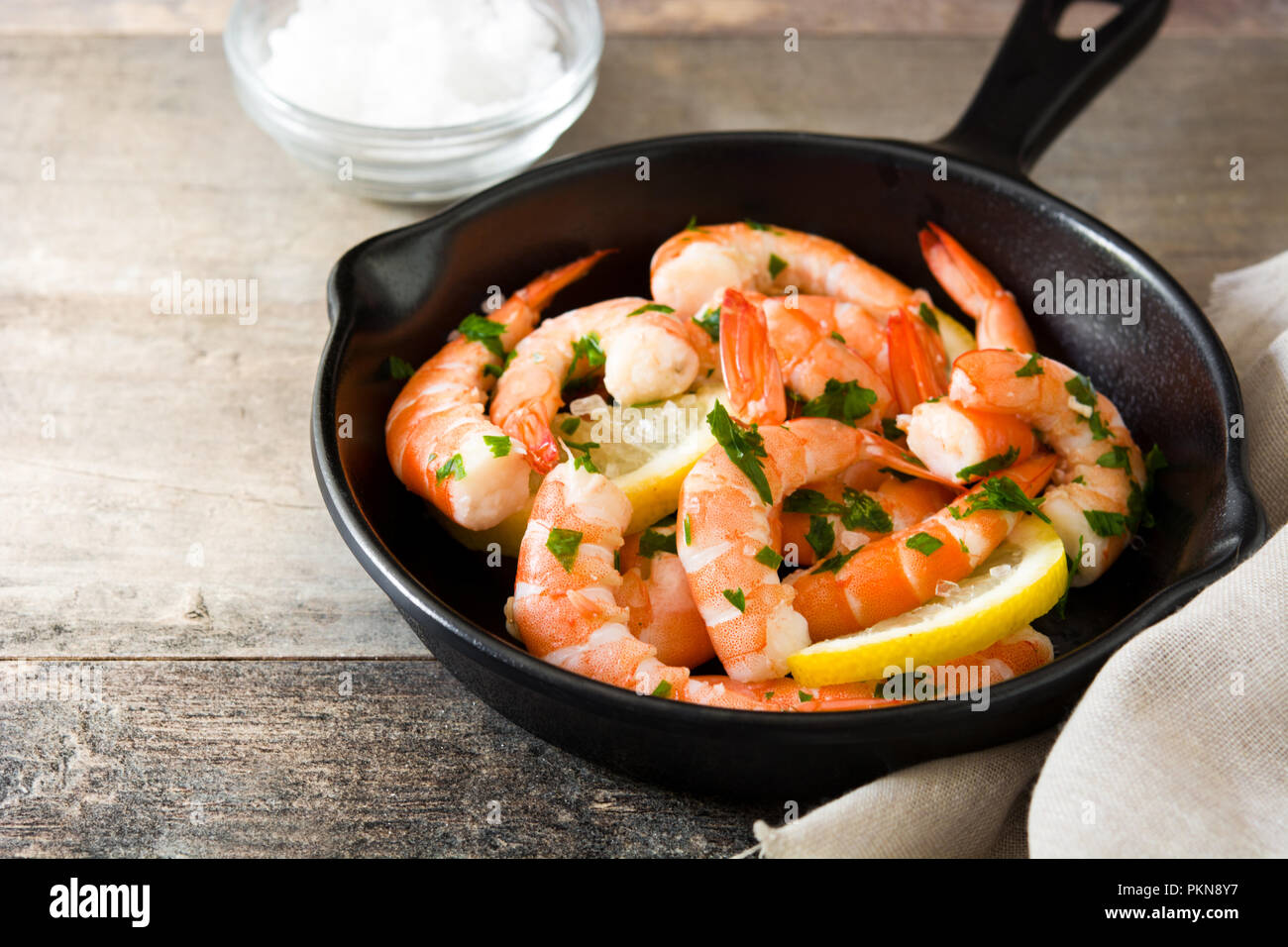 Gegrillte Garnelen, Petersilie und Zitrone in eiserne Pfanne auf hölzernen Tisch Stockfoto