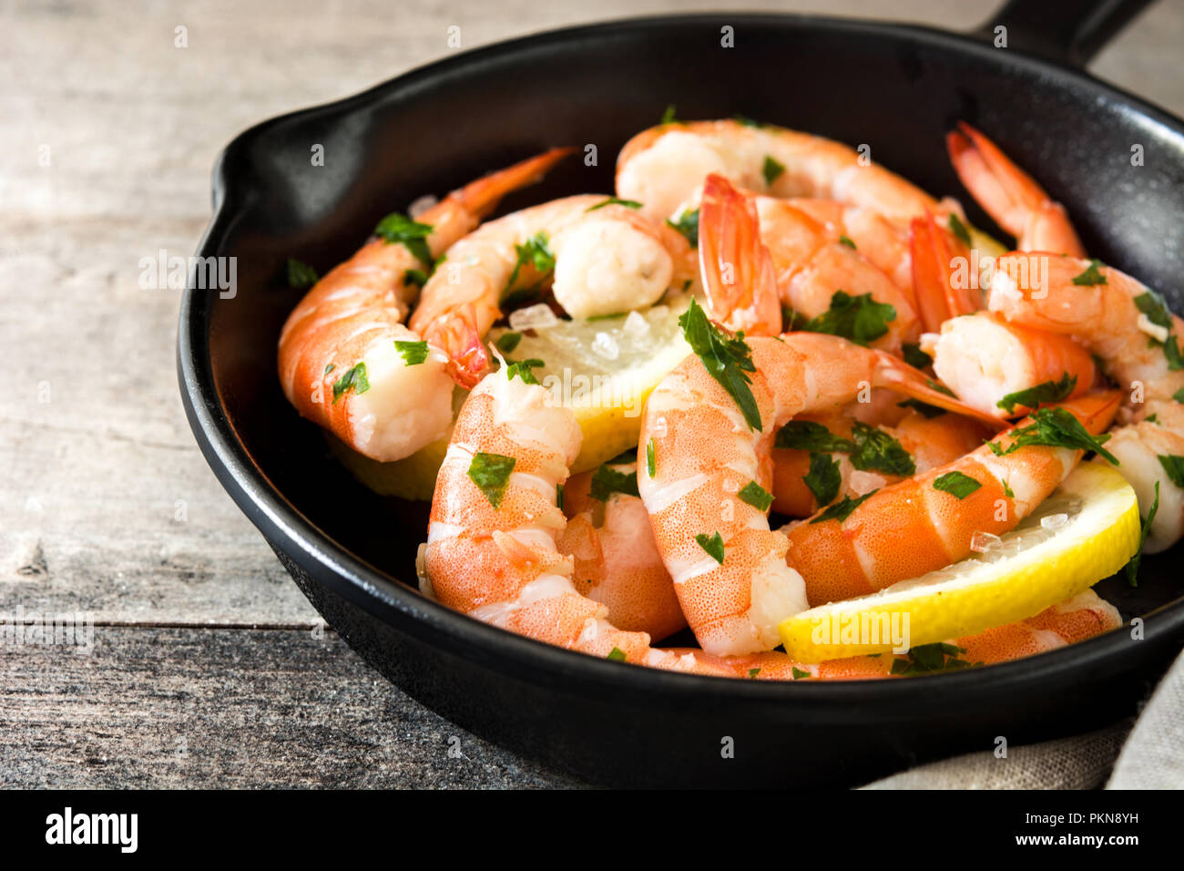 Gegrillte Garnelen, Petersilie und Zitrone in eiserne Pfanne auf hölzernen Tisch Stockfoto