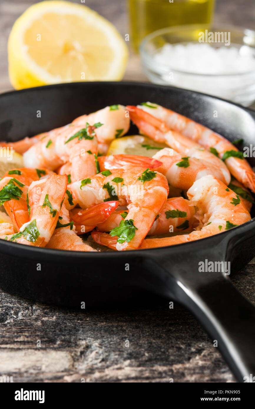 Gegrillte Garnelen, Petersilie und Zitrone in eiserne Pfanne auf hölzernen Tisch Stockfoto