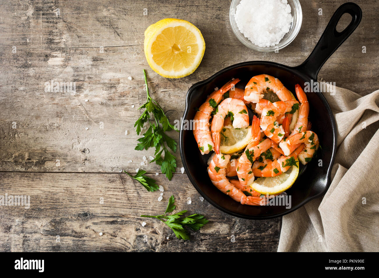 Gegrillte Garnelen, Petersilie und Zitrone in eiserne Pfanne auf hölzernen Tisch. Ansicht von oben. Copyspace Stockfoto