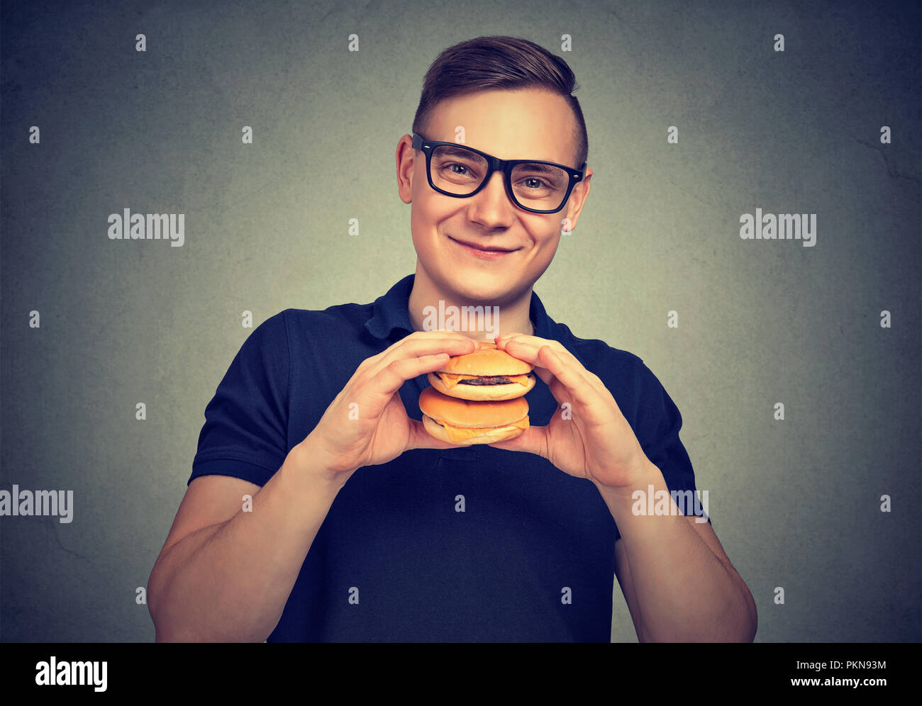 Junge lächelnde Mann in Gläser holding Paar Burger und lächelnd an der Kamera fast food genießen. Stockfoto