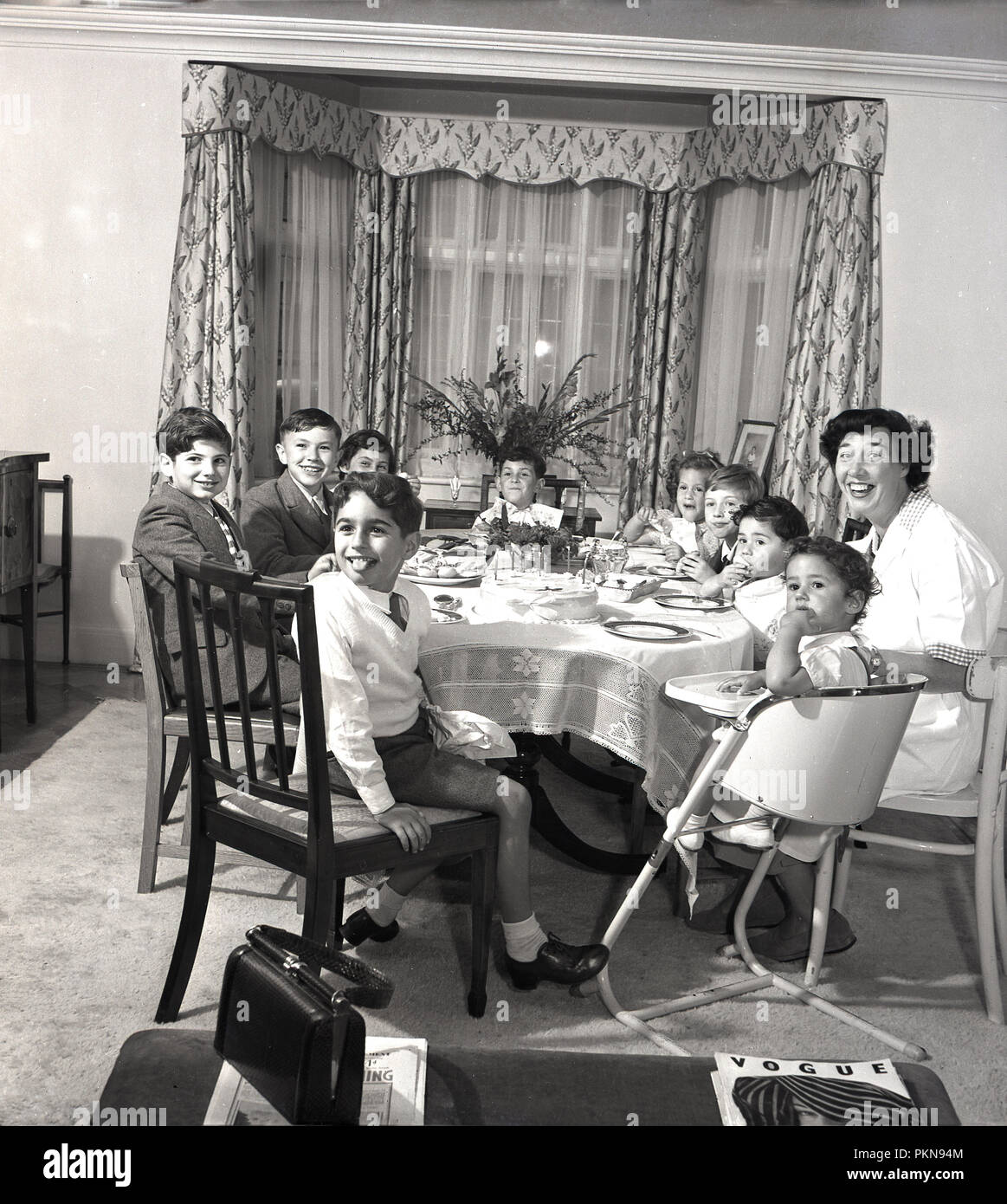 1950er Jahre, historische, Kaffee Kinder - Zeit ... eine glückliche Mutter genießen Nachmittagstee um einen Esstisch mit einer Gruppe von neun jungen Kinder, England, UK. Stockfoto