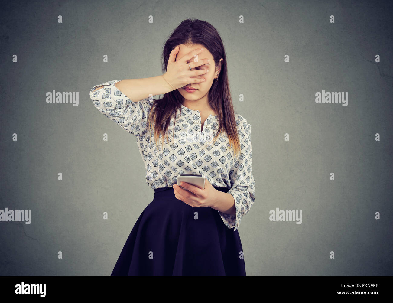 Junge Frau, die Fehler bei der Verwendung von Smartphone und traurig auf grauem Hintergrund Stockfoto