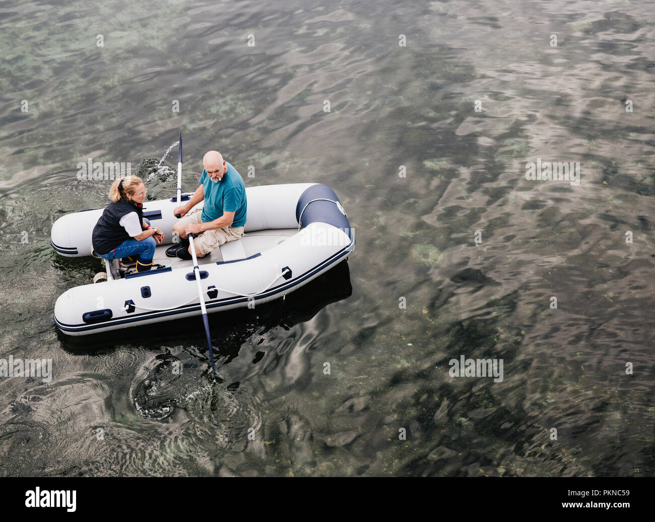 Auf der Suche nach unten von oben auf ein älteres Paar Rudern ein Beiboot in einem ruhigen Meer, Fluss oder See mit Kopie Raum Stockfoto