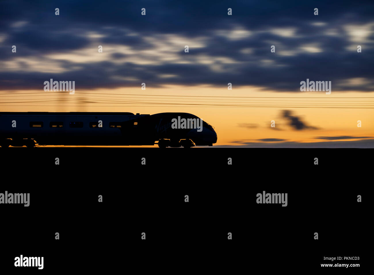 Ein Virgin Trains Westküste Pendolino train eine Silhouette bei Sonnenuntergang auf der West Coast Main Line und Geschwindigkeit. Stockfoto
